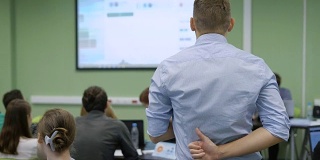 给学生上课的讲师正在用一个麦克风读投影仪上的图像信息，然后是关于大学经济的研讨会。他在背后竖起大拇指