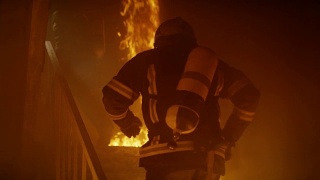 两名勇敢的消防员进入敞开的门，跑上燃烧的楼梯。大楼着火了。到处都是烟雾和明火。在缓慢的运动。视频素材模板下载