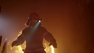 勇敢的消防员在头盔上打开手电筒跑下燃烧的楼梯。火是激烈的。在缓慢的运动。视频素材模板下载