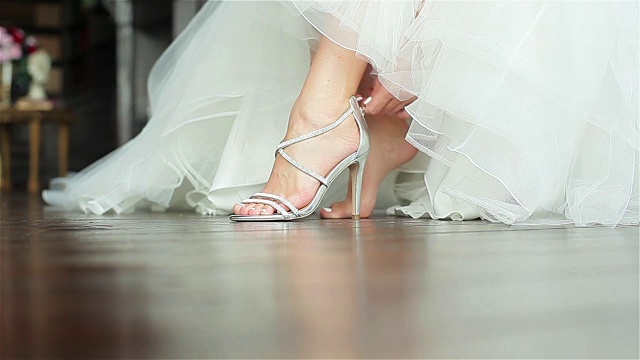 女人穿上鞋，双手合上浅浅的景深。新娘在豪华高跟鞋上系上拉链坐在华丽的白色礼服准备在婚礼上跳舞