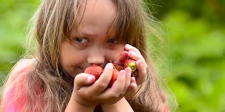 草莓，红扑扑的，熟透了，姑娘闻着甜美的香味，面带微笑。健康的食物