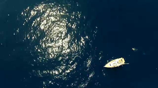 帆船鸟瞰图在蓝色的海洋与阳光闪烁和一个游泳者绕着船