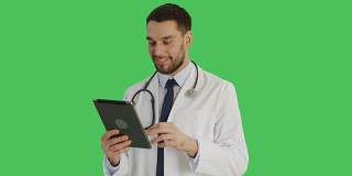 一位英俊医生在平板电脑上做滑动手势的中景。背景为绿幕。