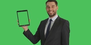 中景一个英俊的商人拿着平板电脑与另一只手做滑动触摸手势。平板电脑和背景都是绿屏。