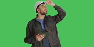 (中景)帅气的工人戴着白色安全帽在平板电脑上做滑动手势。拍摄在绿色屏幕背景。