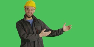 (中景)一个带着安全帽微笑的工人做手势。背景为绿幕。