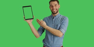 中景一个时尚的男人用一只手拿着平板电脑，用另一只手做滑动触摸手势。平板电脑和背景都是绿屏。