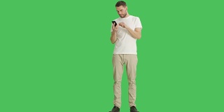 一个漫不经心的男人在他的智能手机上用滑动指向手势的长镜头。背景为绿幕。