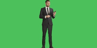 一位英俊的商人用一只手拿着智能手机，用另一只手做滑动触摸手势。平板电脑和背景都是绿屏。