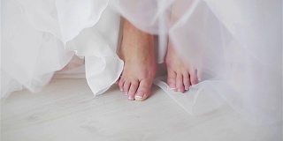 女性的脚与整洁的抛光趾甲接近。没有脸的女人赤脚坐着或站在地板上的细节。连衣裙或裙子的下摆