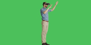 一个英俊的男人戴着虚拟现实眼镜与外部世界互动的长镜头，而相机在他周围旋转。背景为绿幕。