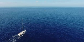 航拍:蓝色大海中的帆船。在地平线上可以看到一艘帆船