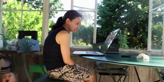 一个女人在电脑屏幕前打呵欠的随意抓拍。三十多岁的母亲在自家阳台上工作。