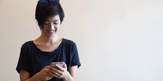 酷酷的亚洲嬉皮女孩与现代外观微笑和大笑，而使用智能手机