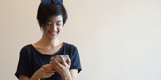 酷酷的亚洲嬉皮女孩与现代外观微笑和大笑，而使用智能手机