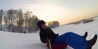 快乐的家伙骑着车，微笑着在雪道上玩雪车。缓慢的运动。雪的冬天的风景。在户外运动