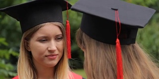两个戴着带流苏的学术帽的年轻女子毕业后交流