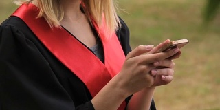 毕业典礼后用智能手机发短信的漂亮金发毕业生