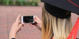 一名女毕业生用手机拍摄她的朋友，并竖起大拇指