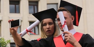 滑稽的学生穿着学术服在手机上自拍，毕业典礼