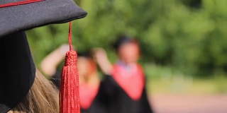 女士戴着学术帽看着快乐的朋友毕业生在公园里玩