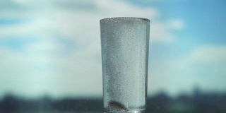 阿斯匹林慢动作地飞溅在玻璃杯里，头痛溶液在模糊的城市背景上。1920 x1080