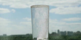 将药丸与水慢动作放入玻璃杯中。阿司匹林喷溅，头痛溶液在模糊的城市背景上。1920 x1080