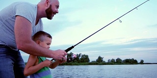 一个男人带着一个孩子去钓鱼，父子俩用旋转杆钓了一条鱼，在湖上进行户外娱乐，渔夫坐在船上，扔钓竿和鱼饵