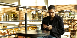 成年男性在咖啡馆里拿着手机喝咖啡