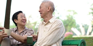 慢镜头亚洲退休夫妇谈论和喝咖啡早上在户外公园