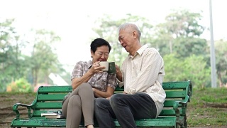 慢镜头快乐的亚洲老夫妇坐在早上的公园喝茶，喝咖啡。交谈并表达爱意视频素材模板下载