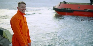 身穿橙色制服的年轻港口工人向正在驶离的轮船挥手
