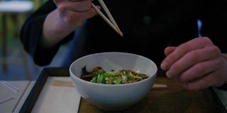 男子的手拿筷子，开始吃面条的特写。蔬菜面在日本餐厅用餐。美味的烤海鲜。