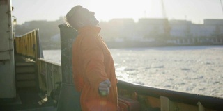 身穿橙色制服的港口工人站在船舷旁。镜头光晕。Slowmotion