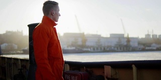 身穿橙色制服的港口工人站在船板旁休息。镜头光晕。Slowmotion