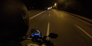 一个骑摩托车的人在傍晚的城镇公路上高速行驶的观点。摩托车在空旷的城市街道上行驶的观点。观点关闭
