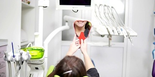 牙科椅上的年轻美女。手术后，她照照镜子。健康微笑的概念。