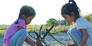 亚洲女孩玩干树枝与姐姐在日落