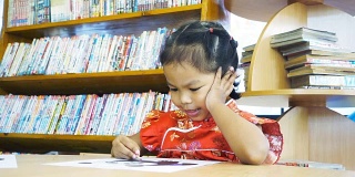 亚洲小女孩穿着中国衣服在图书馆画画