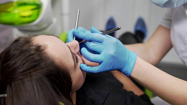 年轻的女牙医正在检查病人的牙齿。近距离观察女牙医的手在手套拿着仪器。牙齿健康和牙齿保健。