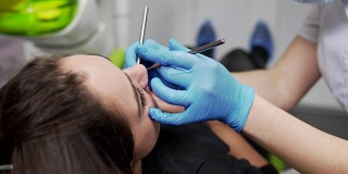 年轻的女牙医正在检查病人的牙齿。近距离观察女牙医的手在手套拿着仪器。牙齿健康和牙齿保健。