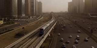 从空中俯瞰蓝色的高速列车，它穿过高速公路上的立交桥，汽车被摩天大楼包围。迪拜,阿联酋
