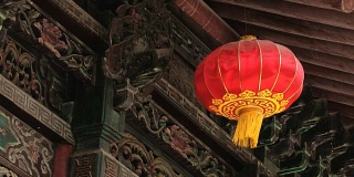 传统的红色中国灯笼挂着一个古老的雕刻和油漆木制建筑背景。