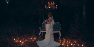 在漆黑的森林里，新娘手捧花束，站在沙发前，点燃蜡烛。