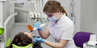 年轻女牙医戴面罩和手套，使用牙科紫外线光设备进行聚合物硬化