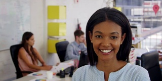 办公室里的一名年轻黑人女性走进焦点，面带微笑