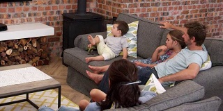 一家人坐在开放式休息室的沙发上看电视