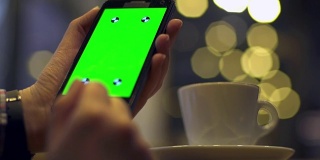 一名女性在咖啡馆拿着绿屏智能手机