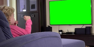 孩子坐在电视机前看儿童节目。绿色色度键屏幕