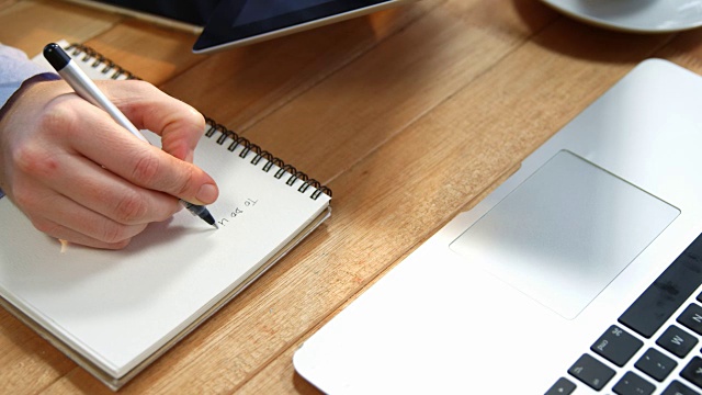 商业女性的手写在笔记本上的桌子上的数字平板电脑和笔记本电脑